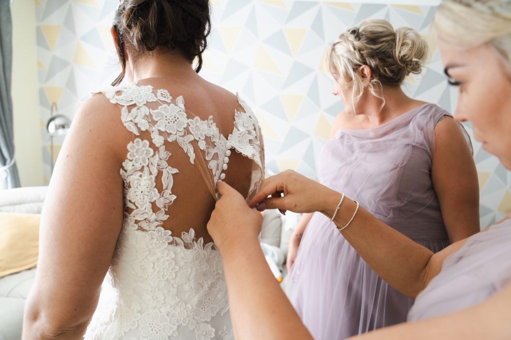 a bridesmaid helps a bride button her wedding dress in her home in hull