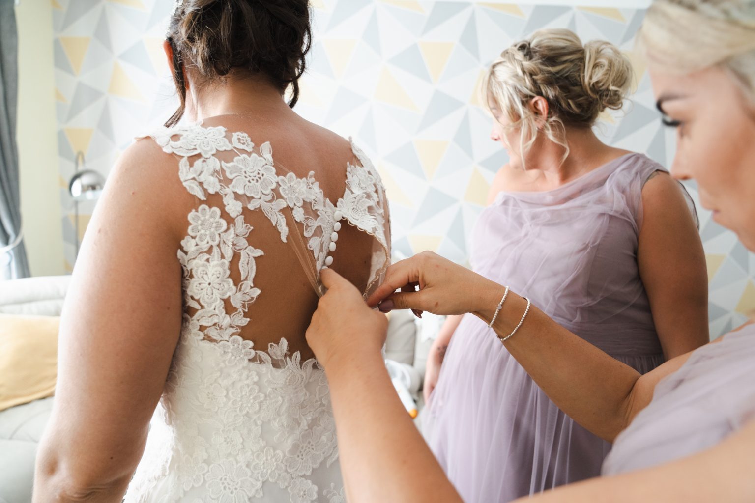 bridesmaid buttons up a brides dress in her home in hull