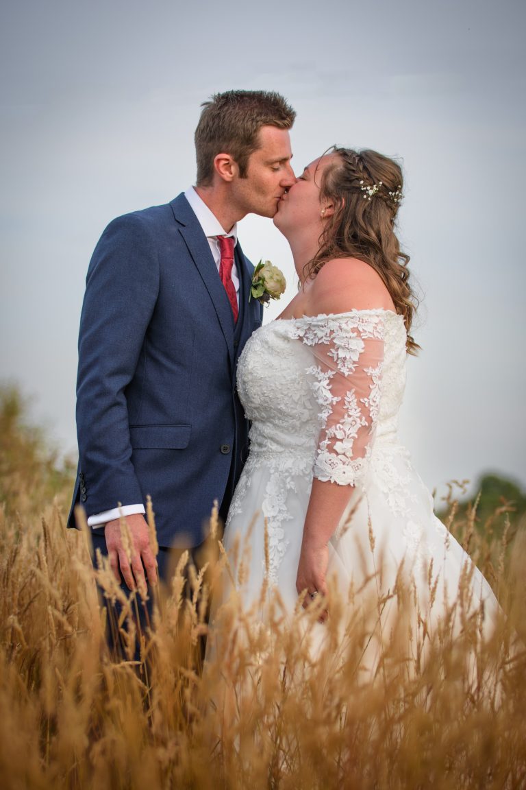 kept photography captures an image of a bride and groom kissing in a field