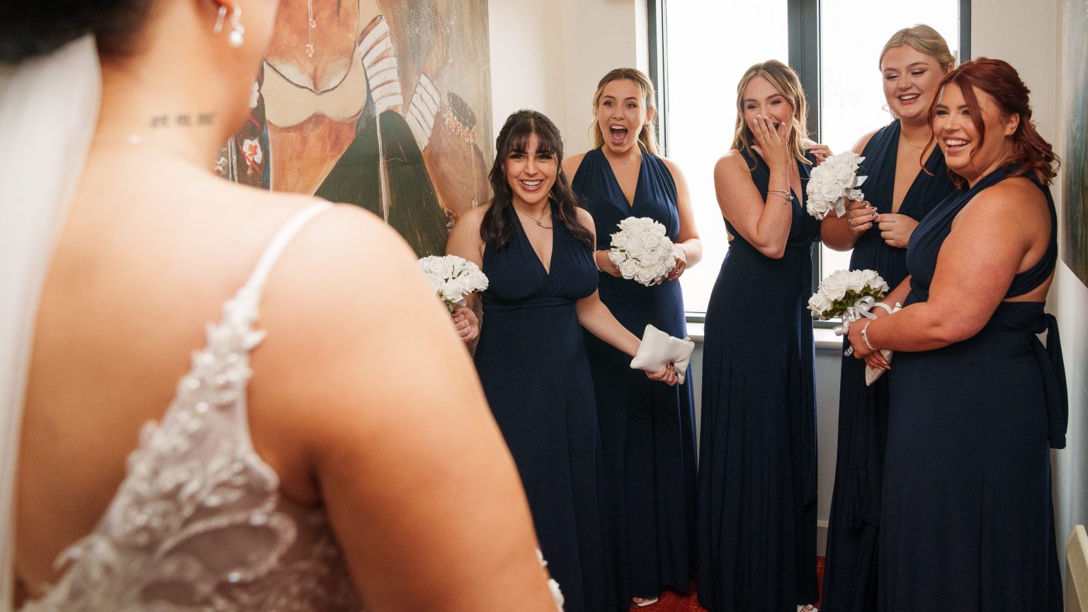 a wedding photograph from a customer's wedding photography gallery; bridesmaids smile and laugh at a dress reveal
