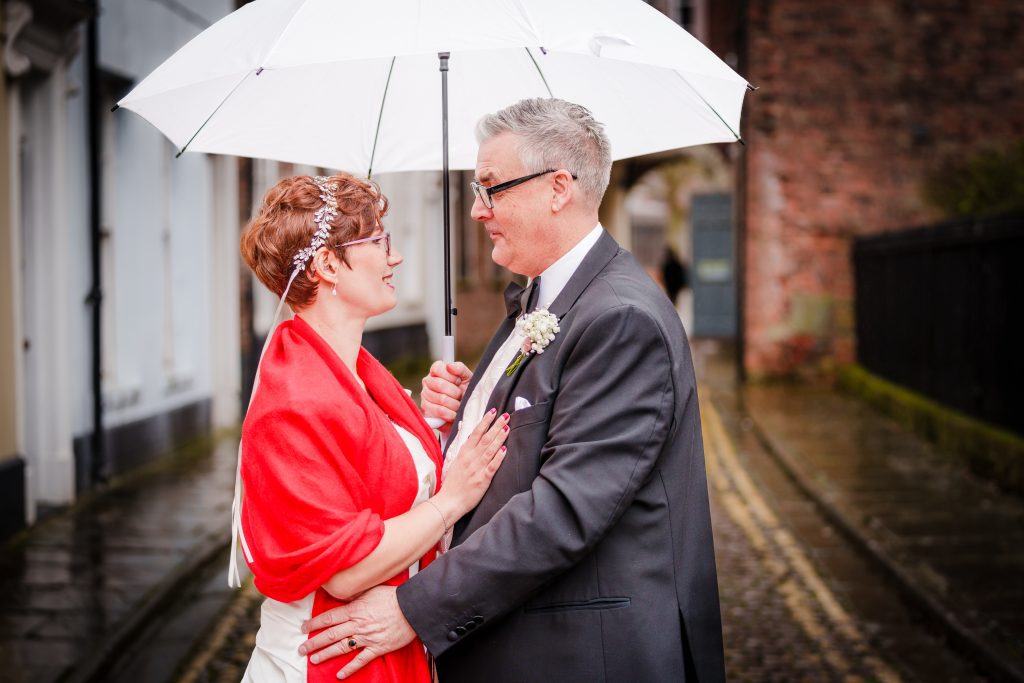 happy wedding couple under umbrella outside minerva masonic lodge scaled