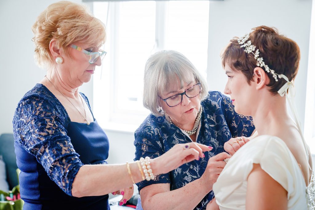 mother of the bride pinning broach on brides dress scaled
