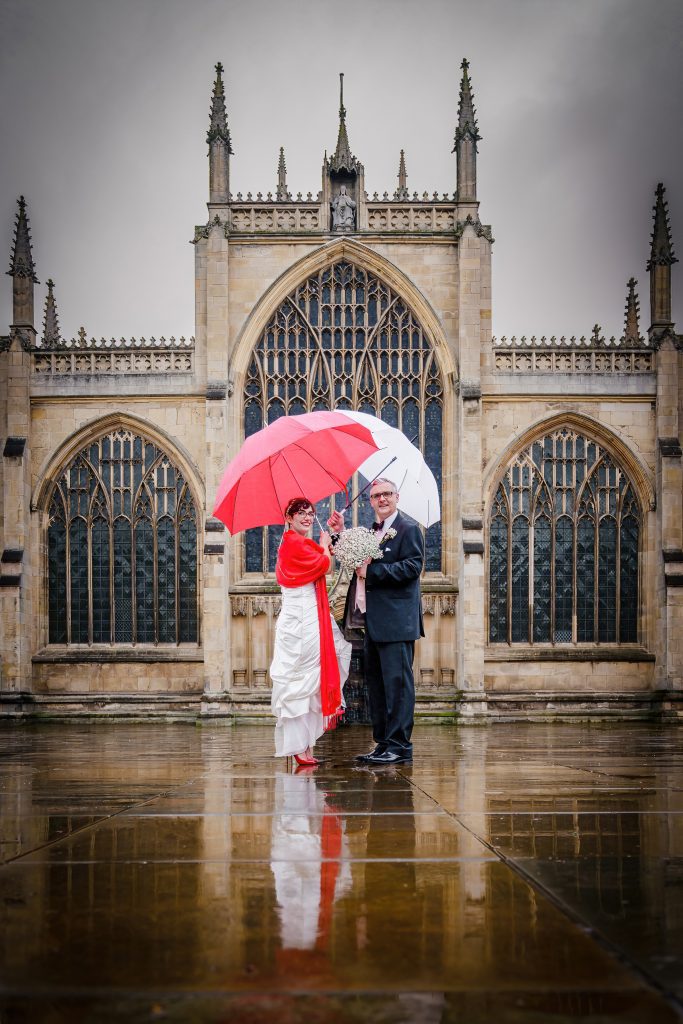 newly married couple outside hull minster after their rainy day wedding ceremony scaled