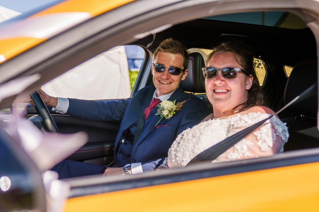 Bride and groom arrive to their reception in a yellow sports car.